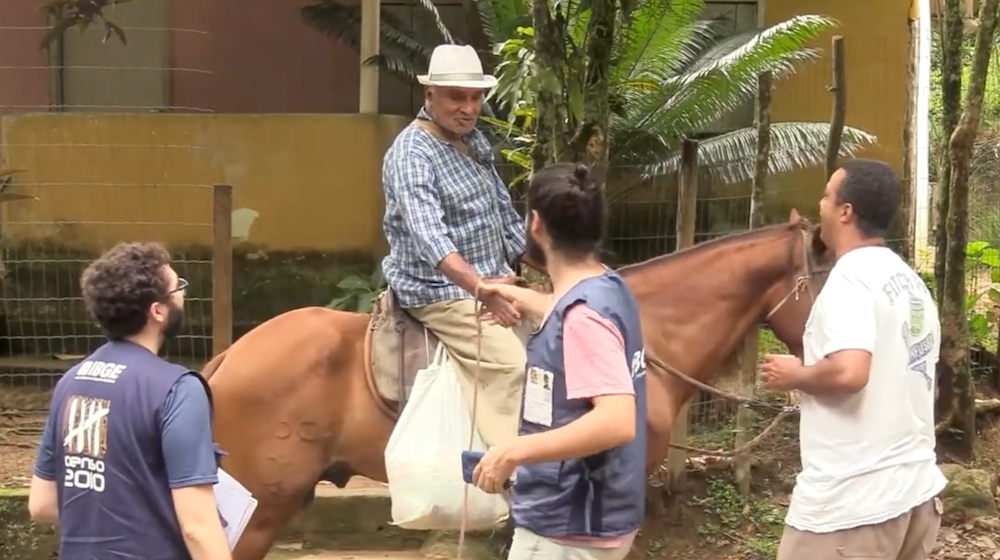 A man on a horse shakes hands with another man, while two men stand nearby.