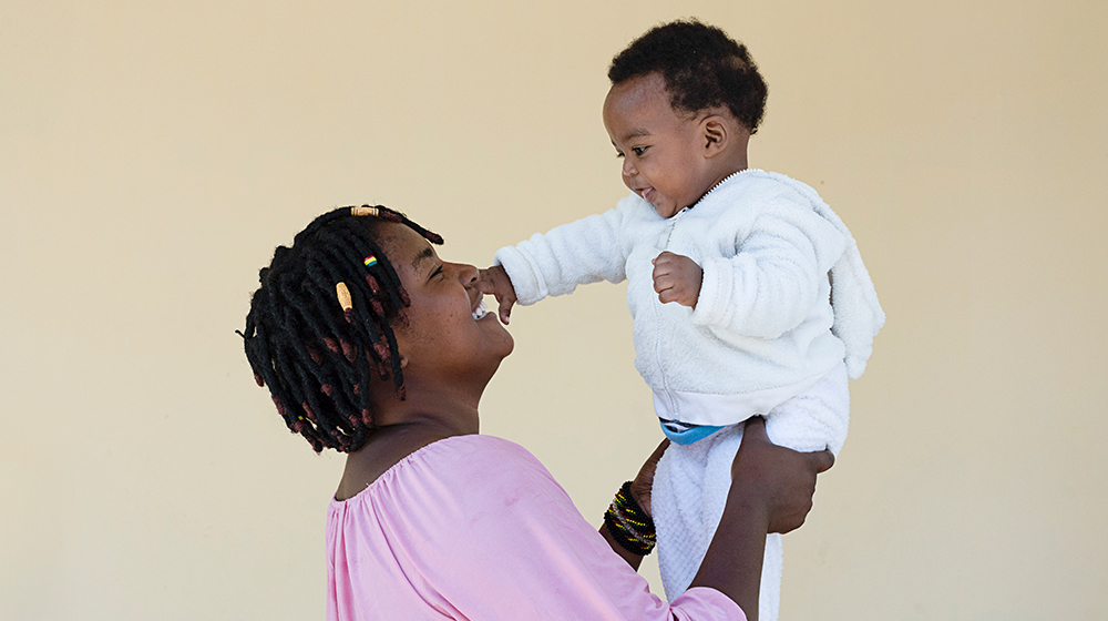 A mother lifts her child up to her face, the child is reaching for the mother's face