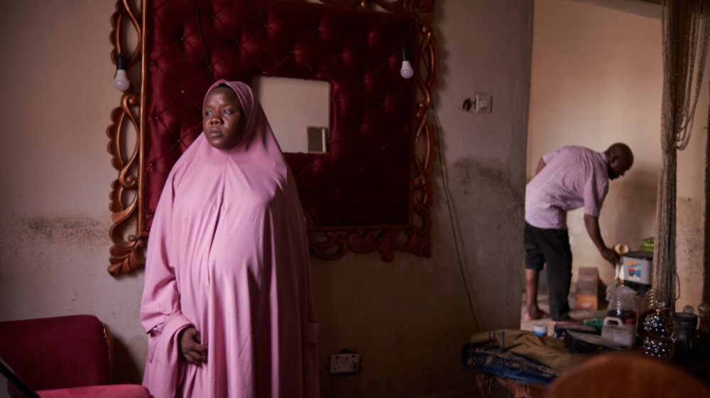 Une femme en tchador rose se tient dans une maison abîmée par les eaux.