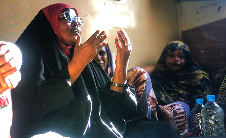 Une femme s’adresse à un groupe de femmes, les mains levées.