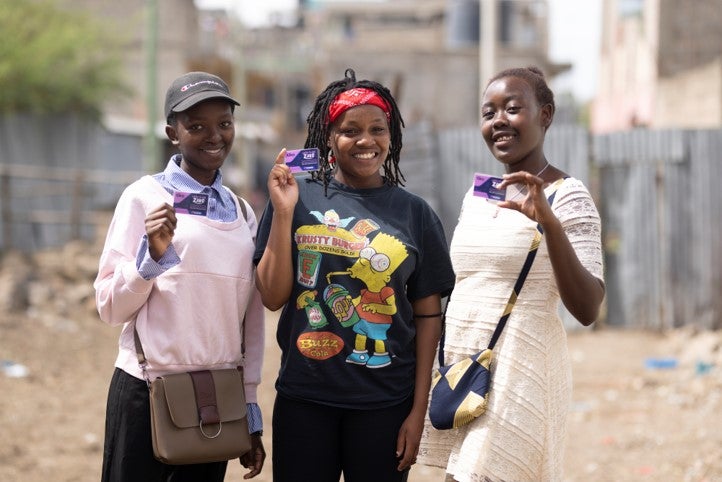 Three adolescent girls stand and smile. 