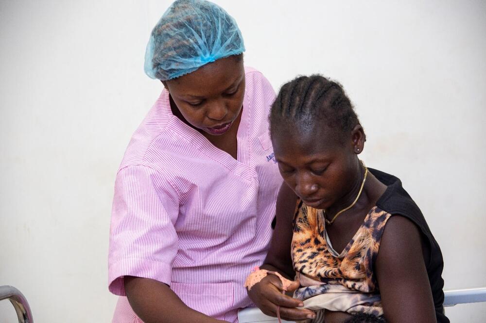 A woman leans over another woman, who holds a baby.