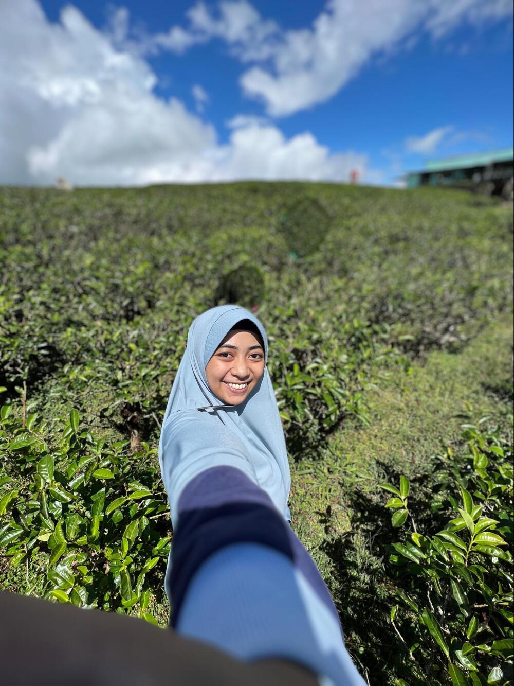 A young woman takes a photo of herself in an outdoor setting.