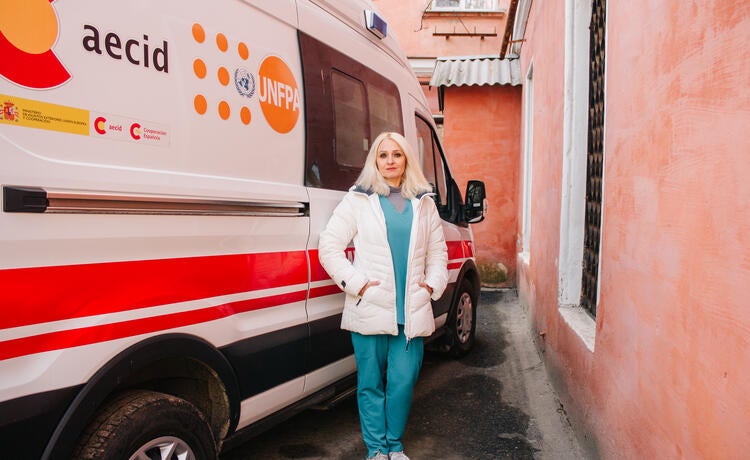 Alt text: A woman stands in front of an ambulance bearing the UNFPA and AECID logos