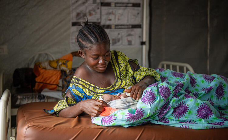 A woman lovingly gazes at her newborn atop a hospital bed.