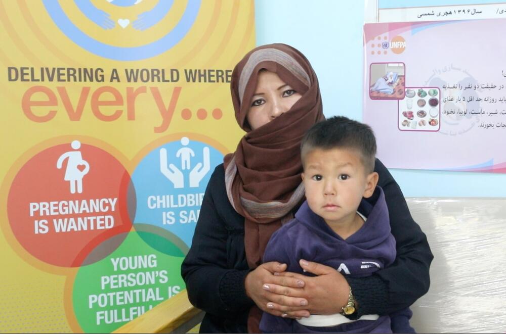 A woman hUna mujer sostiene a un niño frente a un cartel del UNFPAolds a young boy in front of a UNFPA poster