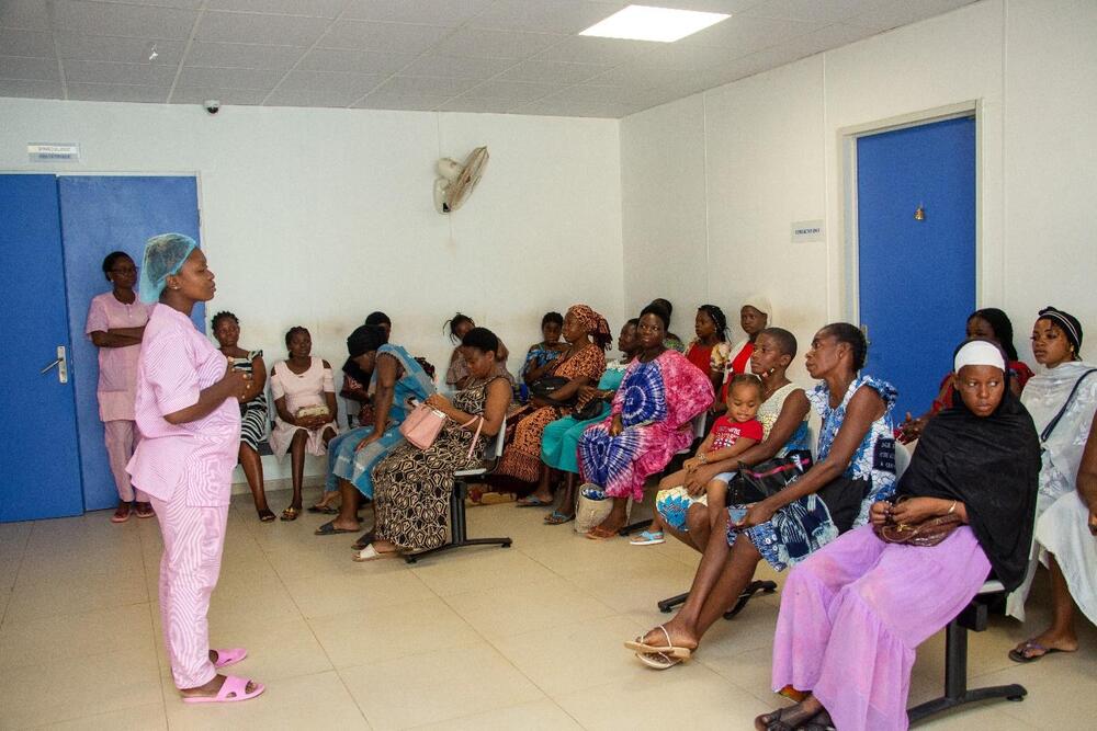 A woman in pink scrubs stands before a group of pregnant women.