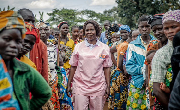  A female health worker in a pink uniform stands outside surrounded by women