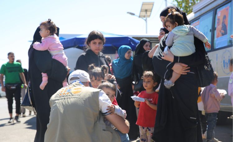  Au premier plan, un homme vêtu d’un gilet de l’UNFPA enlace un enfant. À sa gauche, une femme tient un nourrisson dans ses bras.