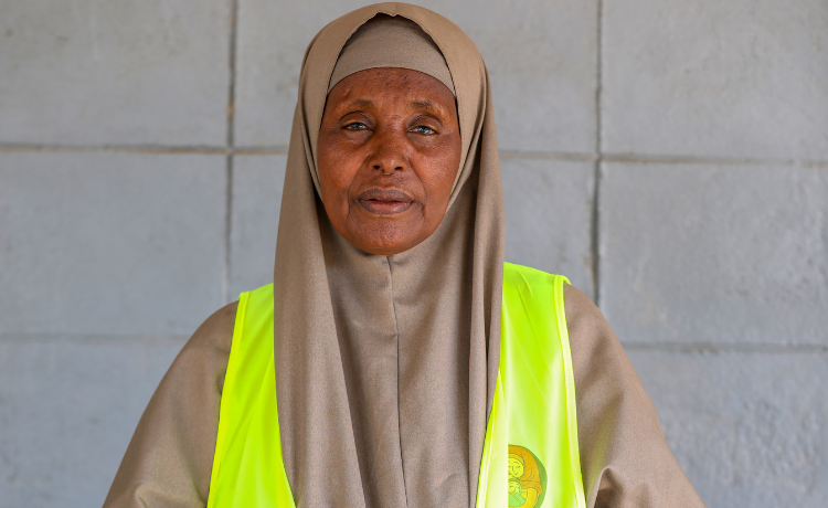 A woman in a yellow high-visibility vest looks into the camera