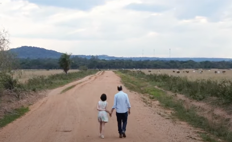 Adolescent girl stands with an older male on a dusty road.