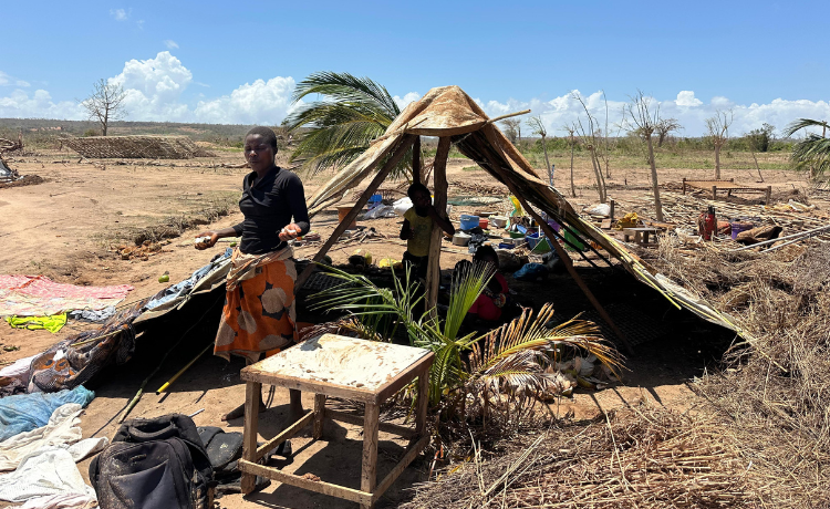 A woman stands in front of a makeshift shelter]