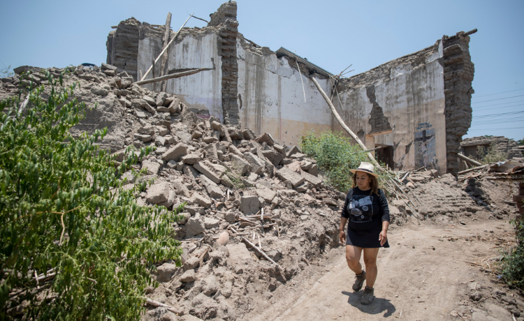 Une femme marche sur un chemin de terre près d’un bâtiment en ruines.