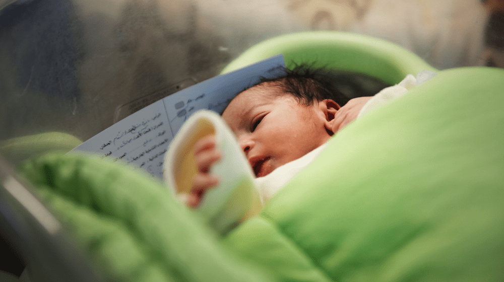 A baby is wrapped in a green blanket in a hospital bassinet.