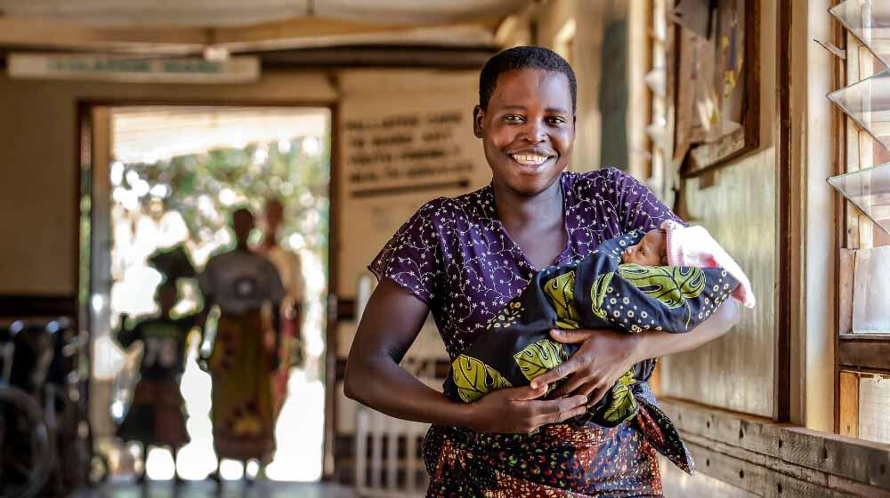 Women smiles into camera while holding a baby.