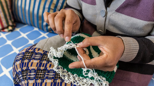 Une jeune femme coud un tissu vert et blanc.