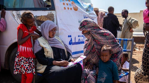 A female health worker takes notes while speaking to a mother sitting with a child